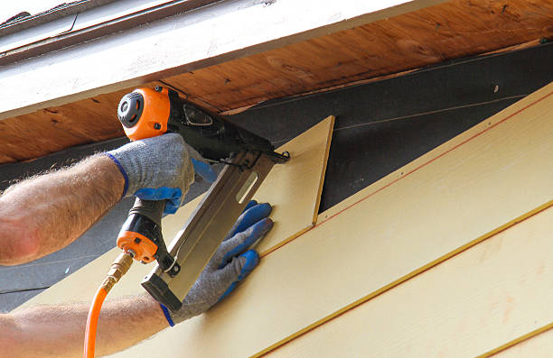 Contractor nailing fiber cement siding panel to residential home exterior