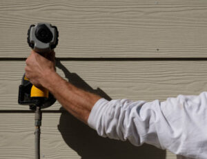 Close-up of worker installing engineered wood siding using power drill